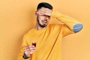 Young hispanic man with beard drinking whiskey shot stressed and frustrated with hand on head,...