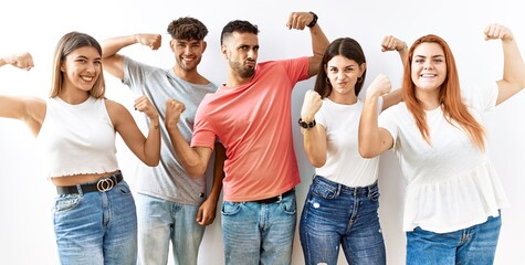 Group of young friends standing together over isolated background showing arms muscles smiling proud. fitness concept.