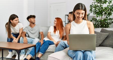Fototapeta premium Group of young friends speaking sitting on the sofa. Woman smilimg happy and using laptop at home.