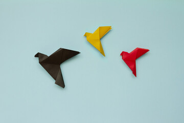 three paper origami pigeons black, yellow, red on light blue background