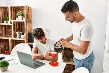 Two hispanic men couple pouring coffee having breakfast at home