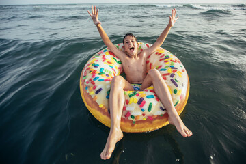Joyful child on inflatable ring ride on breaking wave. Travel lifestyle, swimming activities. Selective focus