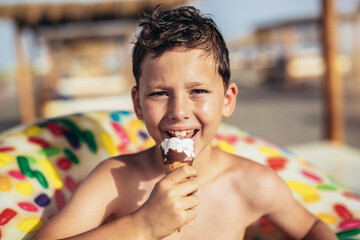 Young boy at the beach eating icecream on a summer day and having fun.