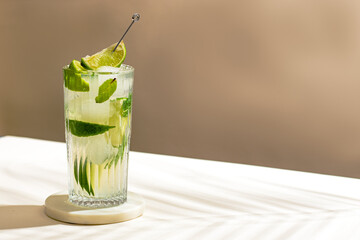 cold Mojito cocktail with rum, lime, ice cubes and mint. Tropical palm leaf shadow. Sunlight and...