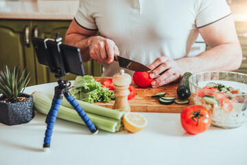 Crop close up of male chef vlogger shoot cooking food vlog blog on smartphone at home kitchen. Man record recipe or tutorial on cell phone preparing healthy vegetarian dish