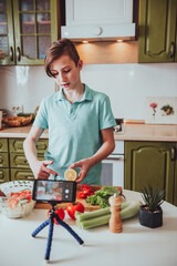 Smiling teenage boy blogger telling his recipe of healthy salad with lemon and vegetables, he shooting himself on video camera