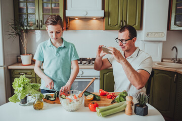 Father and son cook food at home and record videos for blog on social networks. Period of quarantine and self-isolation