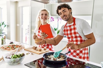 Young couple smiling happy cooking and using touchpad at kitchen.