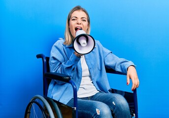 Blonde woman sitting on wheelchair screaming through megaphone over isolated background
