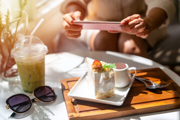 Young woman taking photo of dessert with smart phone for social media in restaurant while traveling
