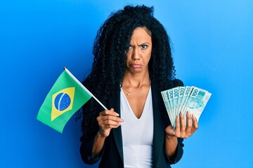 Middle age african american woman holding brazil flag and real banknotes depressed and worry for...