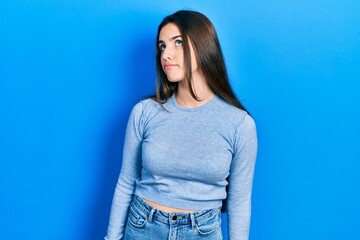Young brunette teenager wearing casual sweater smiling looking to the side and staring away thinking.