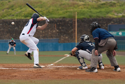 Players playing baseball while standing on field, baseball pitcher throwing ball to batter watched by umpire and catcher