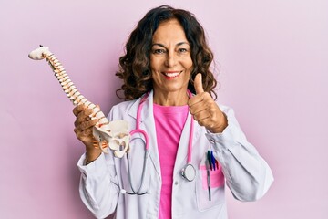 Middle age hispanic doctor woman holding anatomical model of spinal column smiling happy and...
