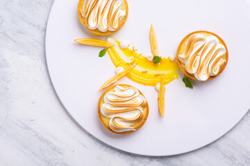 Appetizing lemon tartlets with meringue served on a white plate - obrazy, fototapety, plakaty