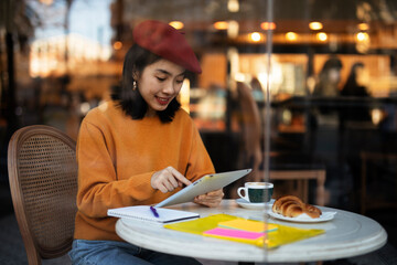 Beautiful Chinese woman drinking coffee in cafe. Young smiling woman using digital tablet in restaurant.