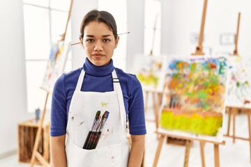 Young brunette woman at art studio relaxed with serious expression on face. simple and natural looking at the camera.