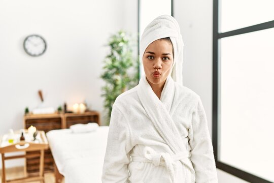 Young brunette woman wearing towel and bathrobe standing at beauty center making fish face with lips, crazy and comical gesture. funny expression.