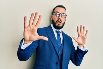 Young man with beard wearing business suit and tie afraid and terrified with fear expression stop gesture with hands, shouting in shock. panic concept. - obrazy, fototapety, plakaty
