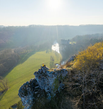 Aerial view of a woman sitting on the rocks with Walzin castle in background at sunset, Dinant, Namur, Belgium.