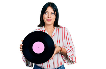Young hispanic girl holding vinyl disc smiling looking to the side and staring away thinking.