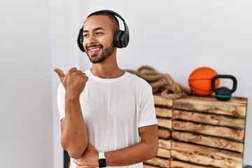African american man listening to music using headphones at the gym smiling with happy face looking...