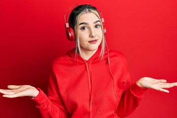 Young modern girl wearing gym clothes and using headphones clueless and confused expression with arms and hands raised. doubt concept.