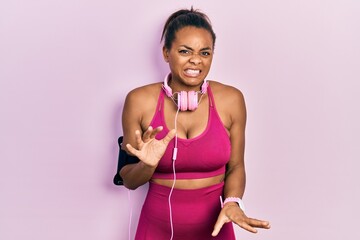 Fototapeta na wymiar Young african american girl wearing gym clothes and using headphones disgusted expression, displeased and fearful doing disgust face because aversion reaction.