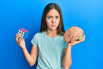 Beautiful brunette little girl playing colorful puzzle cube intelligence game and holding brain...
