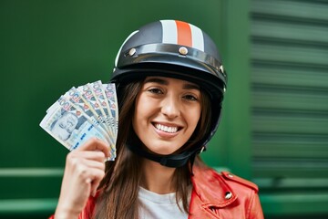 Young hispanic woman wearing moto helmet and holding peruvian sol banknotes at the city.