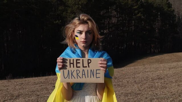 Help Ukraine! Stop War! Woman with protest sign. National symbol of Ukraine. Lady with blood makeup hold patriotic nameplate. Stand with Ukraine, support and solidarity. No war!
