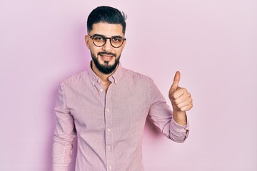 Handsome man with beard wearing casual shirt and glasses smiling happy and positive, thumb up doing excellent and approval sign