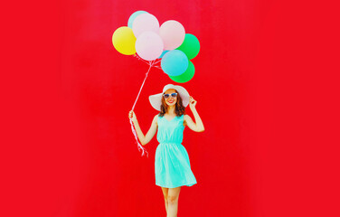 Happy young woman with bunch of colorful balloons on red background