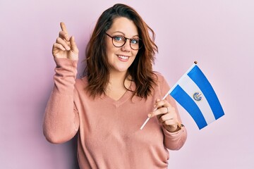 Young caucasian woman holding el salvador flag smiling with an idea or question pointing finger with happy face, number one
