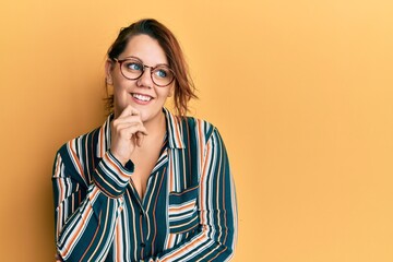 Young caucasian woman wearing casual clothes and glasses with hand on chin thinking about question, pensive expression. smiling with thoughtful face. doubt concept.