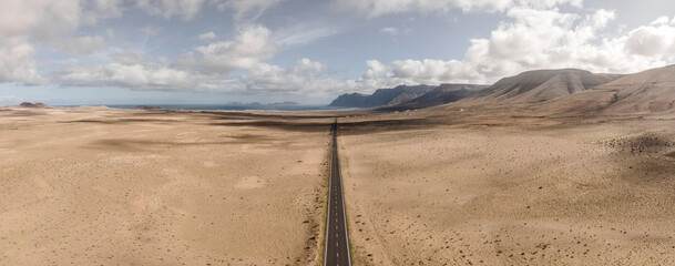 Aerial panoramic view of a straight road crossing the desert valley near Teguise, Lanzarote, Canary Islands, Spain.