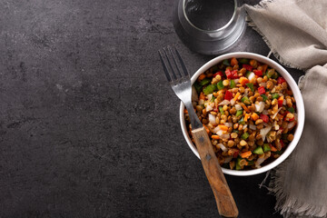 Lentil salad with peppers,onion and carrot in a bowl on black background. Top view. Copy space