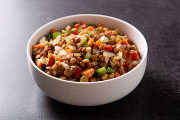 Lentil salad with peppers,onion and carrot in a bowl on black background
