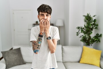 Hispanic man with beard at the living room at home laughing and embarrassed giggle covering mouth...