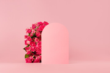 Spring fresh pink roses as arch with empty rounded door as podium for presentation cosmetic products or goods, mockup on pastel pink background, copy space. Template for advertising, design, card.