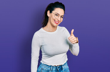 Young hispanic woman wearing casual clothes doing happy thumbs up gesture with hand. approving...