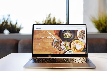 Background image of opened laptop with Food delivery website on table in cafe, copy space