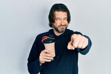 Middle age caucasian man wearing sport clothes drinking a protein shake pointing with finger to the...