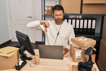 Handsome middle age man working at small business ecommerce wearing headset with angry face, negative sign showing dislike with thumbs down, rejection concept