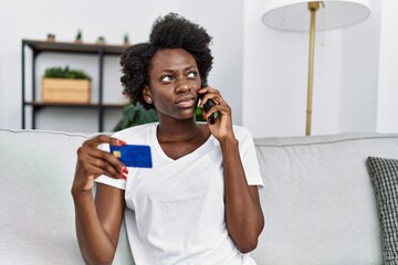 Young african american woman speaking on the phone holding credit card at home