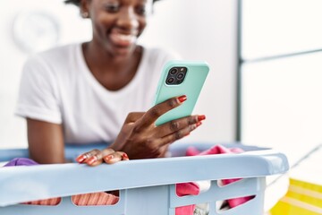 Young african american woman using smartphone doing laundry at laundry