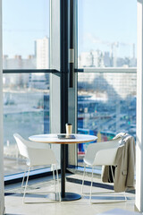 Vertical background image of minimal cafe setup against floor to ceiling windows with urban city skyline in background