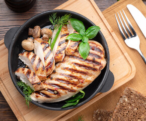 Roasted chicken fillet and mushrooms with herb in the frying pan on the wooden table close-up.