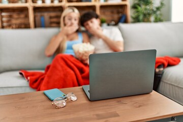 Young couple watching film and eating popcorn sitting on the sofa at home.