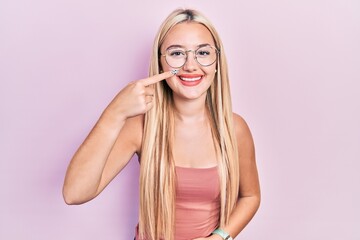 Young blonde girl wearing casual clothes pointing with hand finger to face and nose, smiling cheerful. beauty concept